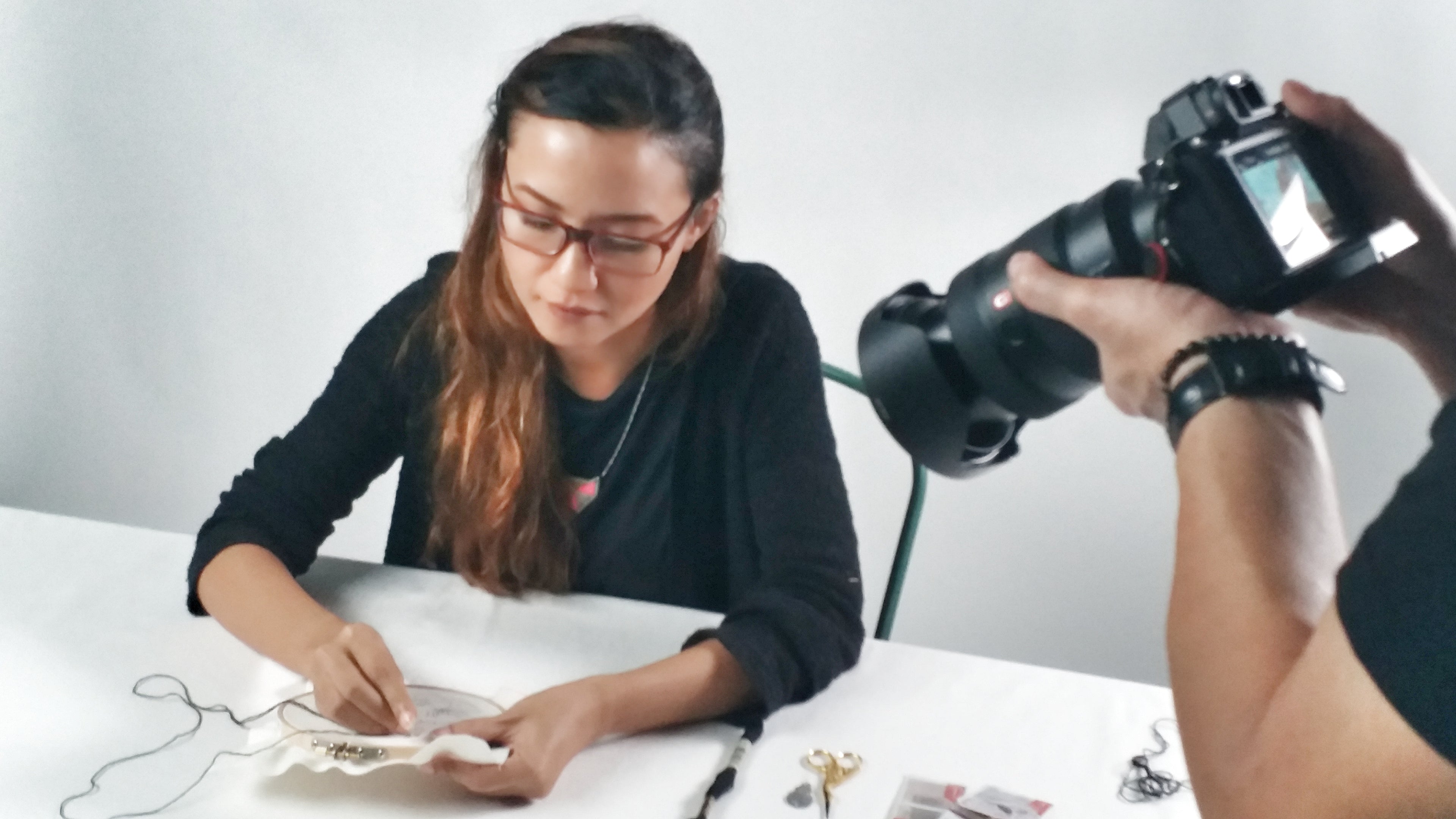 Person taking a photograph of another person working on a project with a camera.