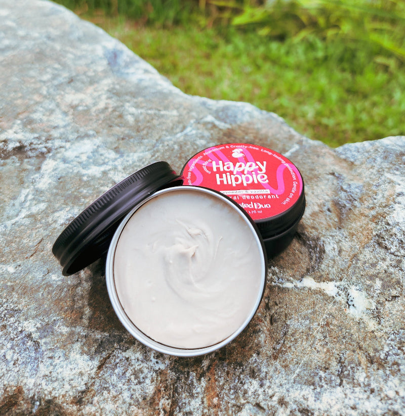 2 jars of natural deodorant on a rock in the outdoors with one jar opened